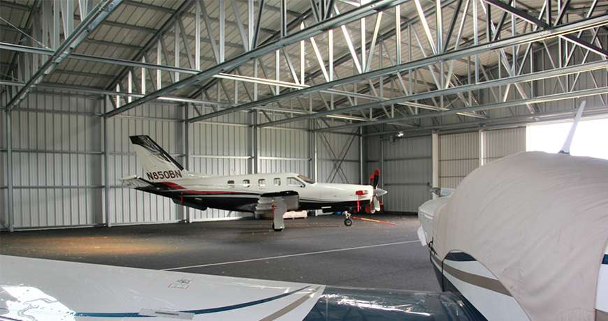 White and blue business jet parked inside a steel dry and safe metal building.
